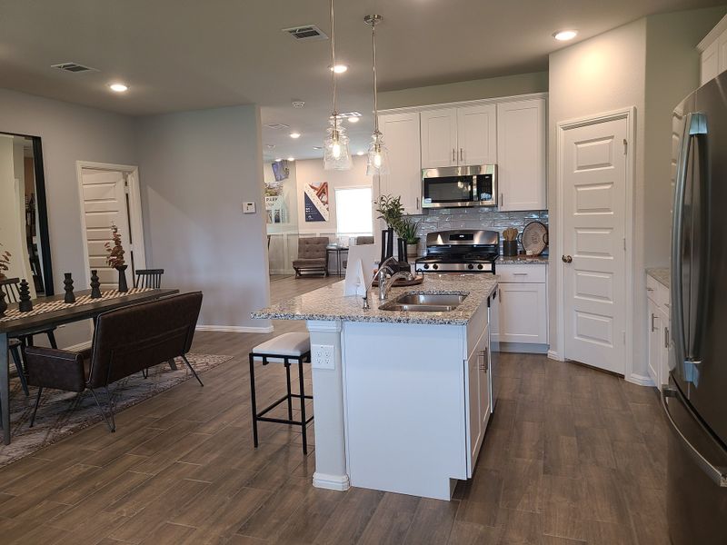 A modern kitchen with granite countertops, stainless steel appliances, and elegant lighting, adjacent to a cozy dining area.