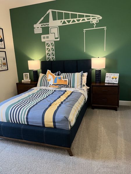 A playful kids' room with construction-themed decor, featuring a green accent wall and cozy bedding.