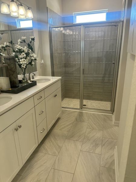 A sleek bathroom with a glass-enclosed shower, dual sinks, and elegant tile flooring enhanced by stylish lighting.