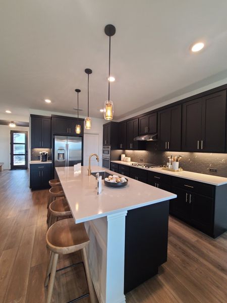 A modern kitchen featuring sleek dark cabinets, a long island with barstools, and stylish pendant lighting.