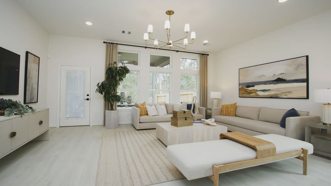 Luxurious living room boasts modern chandelier, expansive windows, and refined décor in The Woodlands Hills.