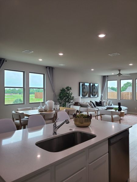 A modern open-concept living space with a bright kitchen and cozy seating area, featuring large windows and sleek design.