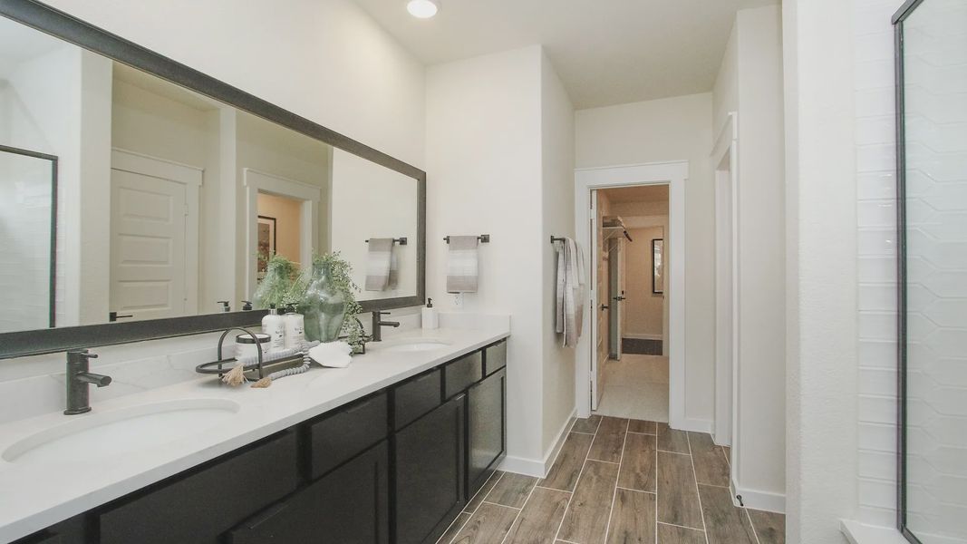 Luxurious bathroom features sleek black cabinetry, expansive mirror, and exquisite wood flooring. Colony at Pinehurst.