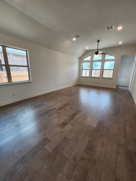 A spacious living room with vaulted ceilings, large windows, and rich wood flooring.