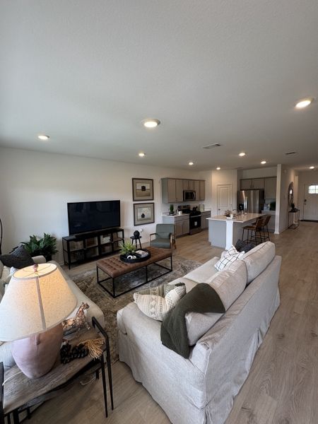 A cozy living area with a soft gray sofa, modern coffee table, large TV, and open kitchen layout.