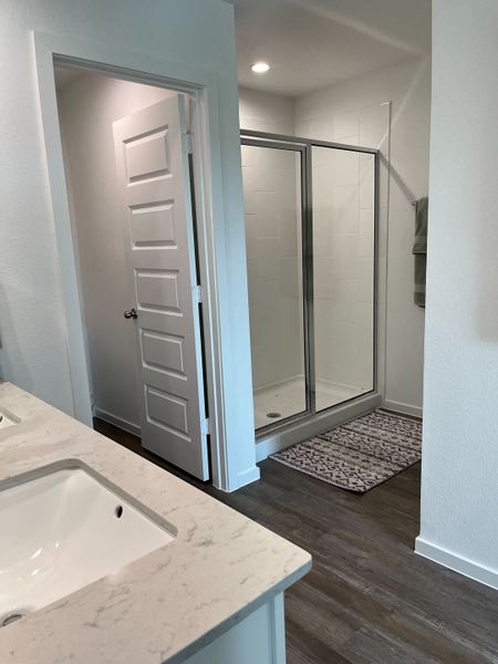 A modern bathroom featuring dual sinks, wood flooring, and a spacious glass shower with elegant tile accents.