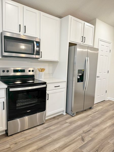 A modern kitchen with stainless steel appliances, white cabinetry, and wood-style flooring.