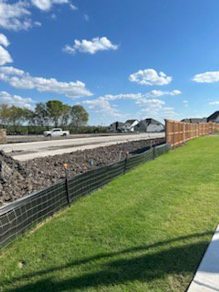Construction site view with lush green grass in Hillstead 60' by Perry Homes, Lavon, TX, under a clear blue sky.