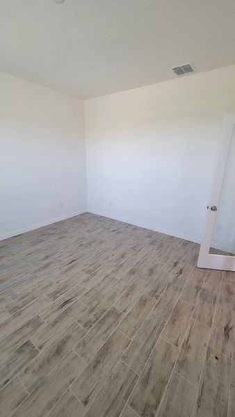 A spacious room with light wood-look tile flooring and pristine white walls, offering a modern and airy atmosphere.