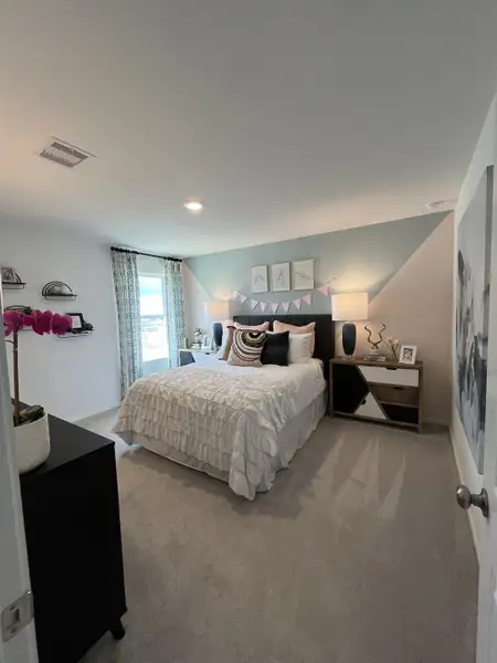 A cozy bedroom featuring a ruffled comforter, geometric accent wall, and modern decor in soft tones.