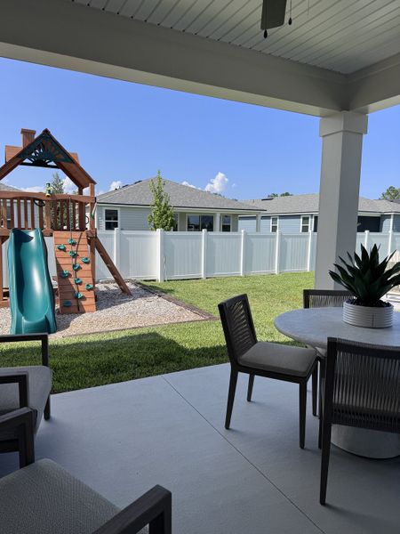 A cozy patio with outdoor seating overlooks a lush yard and playset, perfect for family fun and relaxation.