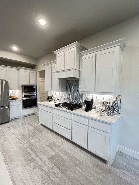 A modern kitchen with sleek white cabinets, mosaic backsplash, and built-in stainless steel appliances.