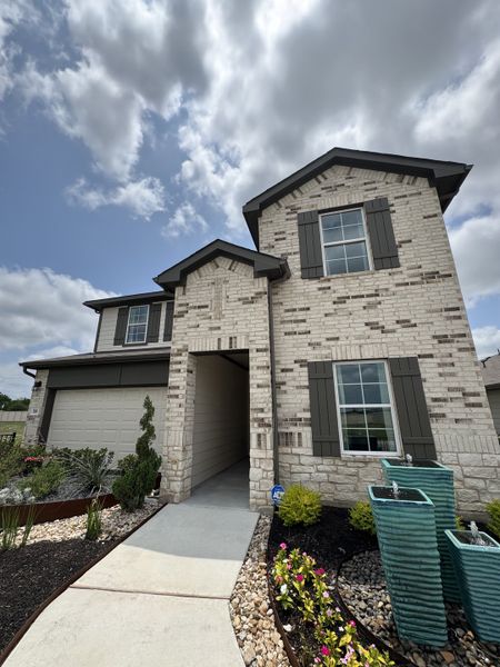 A charming light brick home with dark shutters and landscaped garden in Prairie Lakes by D.R. Horton (Buda, TX).
