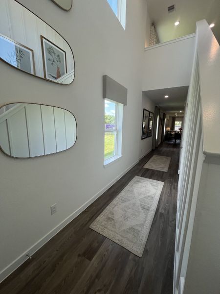 A bright hallway featuring wooden floors, decorative mirrors, and elegant wall art.