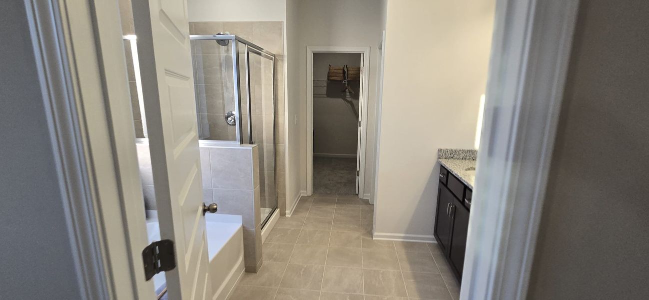 A modern bathroom featuring tiled flooring, a glass shower, and a granite countertop leads to a spacious walk-in closet.