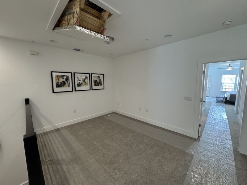 A modern room with neutral carpet, abstract artwork, and a ceiling attic access leading to a bright bedroom. A modern room with neutral carpet, abstract artwork, and a ceiling attic access leading to a bright bedroom.