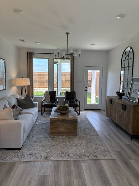 A cozy living room with a white sofa, wooden accents, large window, and elegant chandelier.