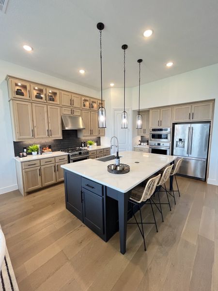 A modern kitchen with neutral cabinets, sleek appliances, a large island, and pendant lighting. A modern kitchen with neutral cabinets, sleek appliances, a large island, and pendant lighting.