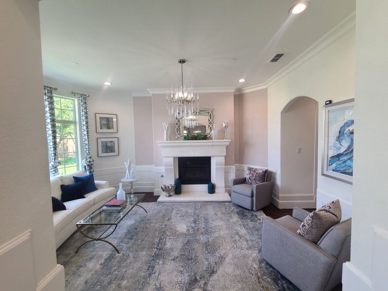 A cozy living room featuring a chic chandelier, elegant fireplace, plush seating, and large windows. A cozy living room featuring a chic chandelier, elegant fireplace, plush seating, and large windows.