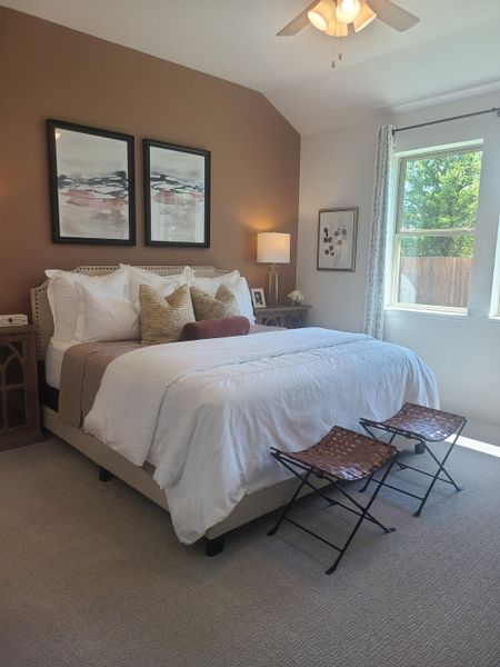 A cozy bedroom featuring a plush bed, warm accent wall, stylish artwork, and ample natural light from a large window.