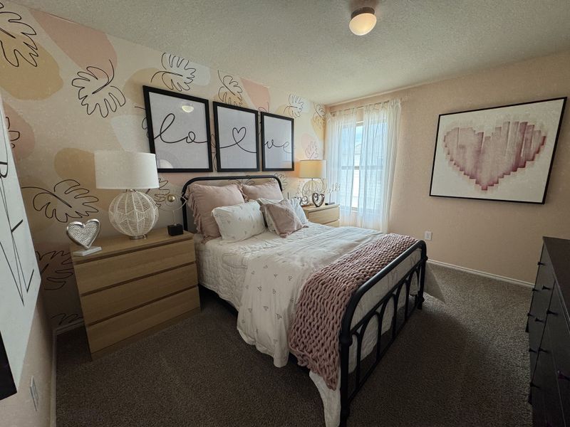 A cozy bedroom featuring artistic wall decor, soft pink accents, and abundant natural light.