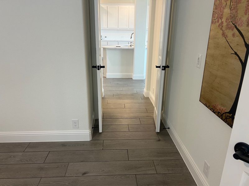 A modern hallway with sleek wood flooring, white walls, and a glimpse of a bright kitchen area. A modern hallway with sleek wood flooring, white walls, and a glimpse of a bright kitchen area.