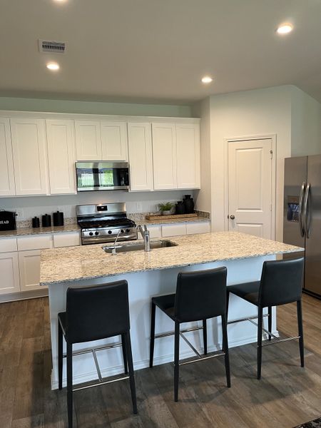 A modern kitchen with sleek white cabinets, granite countertops, a stainless steel oven, and stylish black bar stools. A modern kitchen with sleek white cabinets, granite countertops, a stainless steel oven, and stylish black bar stools.