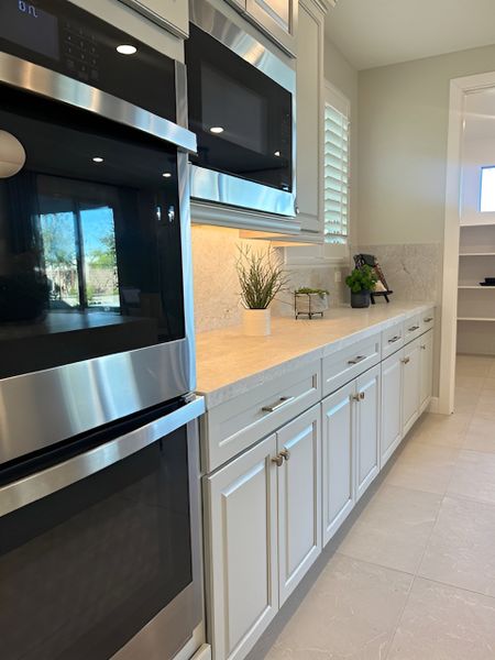 A built-in double oven with white cabinetry, marble countertops, and a stylish backsplash.