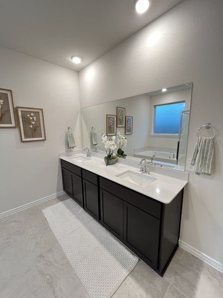 A modern bathroom with dual sinks, dark cabinetry, a large mirror, and tasteful floral decor. A modern bathroom with dual sinks, dark cabinetry, a large mirror, and tasteful floral decor.