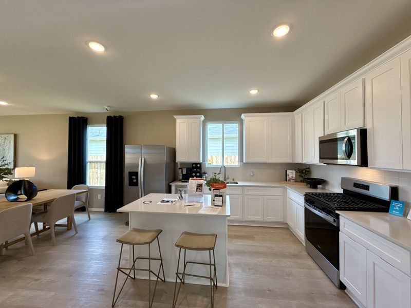 A modern kitchen with white cabinetry, stainless steel appliances, and an inviting dining area with elegant lighting. A modern kitchen with white cabinetry, stainless steel appliances, and an inviting dining area with elegant lighting.