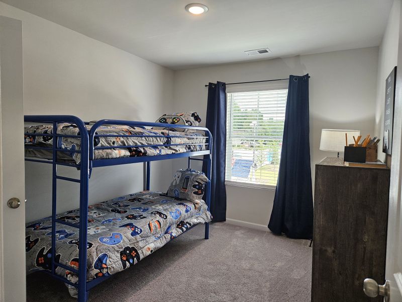 A cozy bedroom featuring a playful bunk bed with game-themed bedding and a view-drawing window with dark drapes.