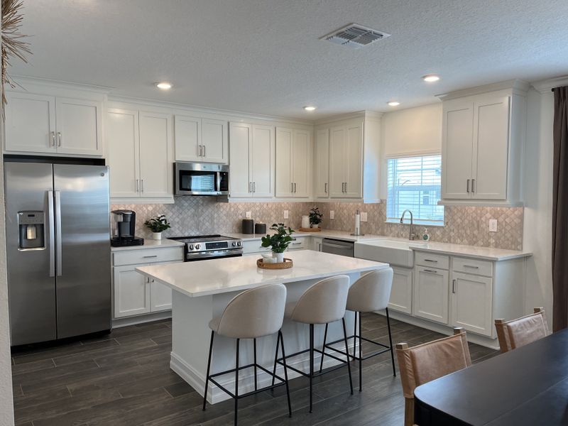 A modern kitchen with white cabinetry, stainless steel appliances, and a large island with seating.