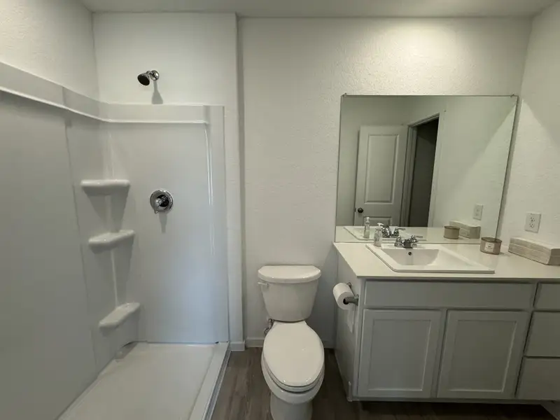 A modern bathroom with a sleek shower, white vanity, large mirror, and wooden flooring. A modern bathroom with a sleek shower, white vanity, large mirror, and wooden flooring.