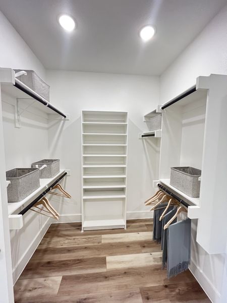 A spacious walk-in closet with sleek shelving, wooden flooring, and ample storage space. A spacious walk-in closet with sleek shelving, wooden flooring, and ample storage space.
