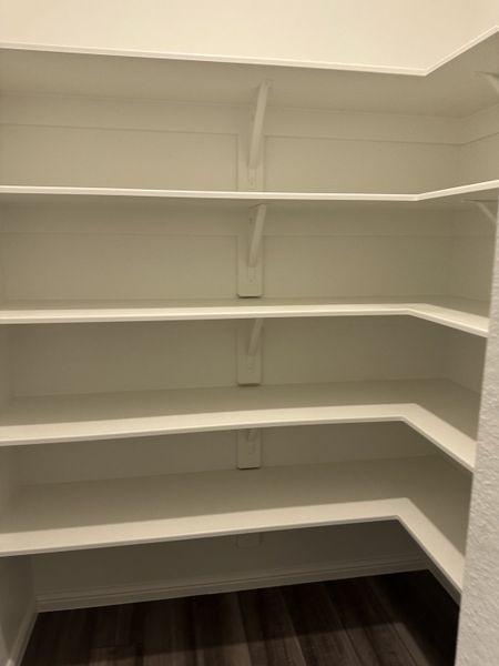 A spacious walk-in pantry with multiple white shelves and dark wood flooring. A spacious walk-in pantry with multiple white shelves and dark wood flooring.