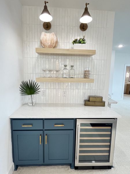 A chic beverage nook with navy cabinets, open shelves, and a wine cooler under elegant wall sconces. A chic beverage nook with navy cabinets, open shelves, and a wine cooler under elegant wall sconces.