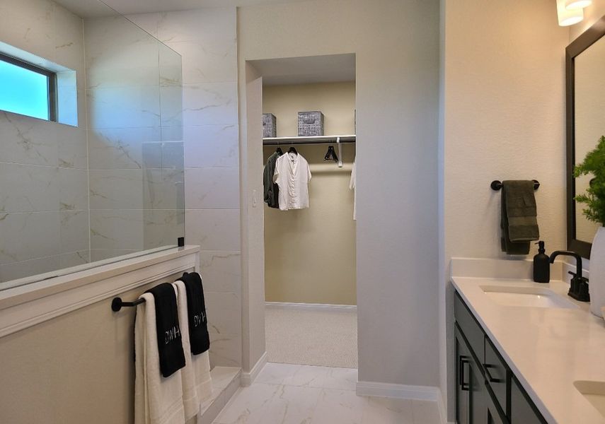 A modern bathroom with dual sinks, glass walk-in shower, and a spacious walk-in closet.
