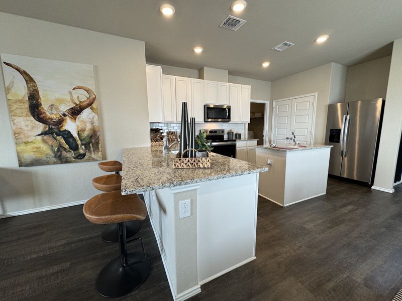 A modern kitchen with granite countertops, sleek stainless steel appliances, and leather bar stools.