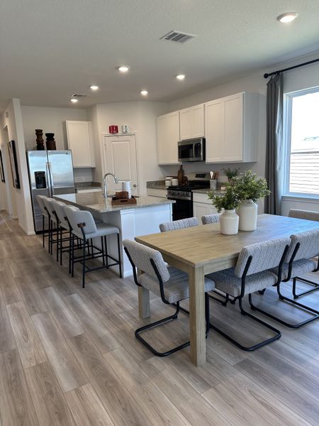 A modern kitchen with a large island, dining table, sleek appliances, and light wood flooring. A modern kitchen with a large island, dining table, sleek appliances, and light wood flooring.