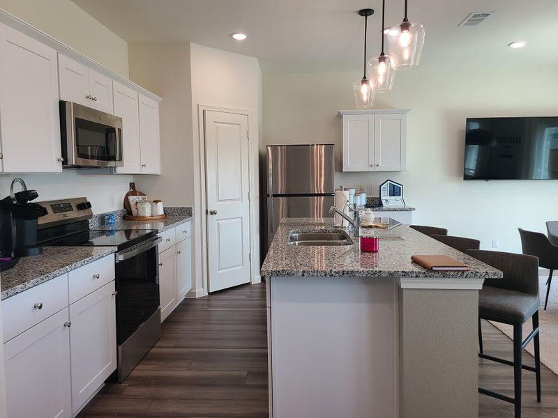 A modern kitchen with granite countertops, white cabinets, pendant lighting, and stainless steel appliances.