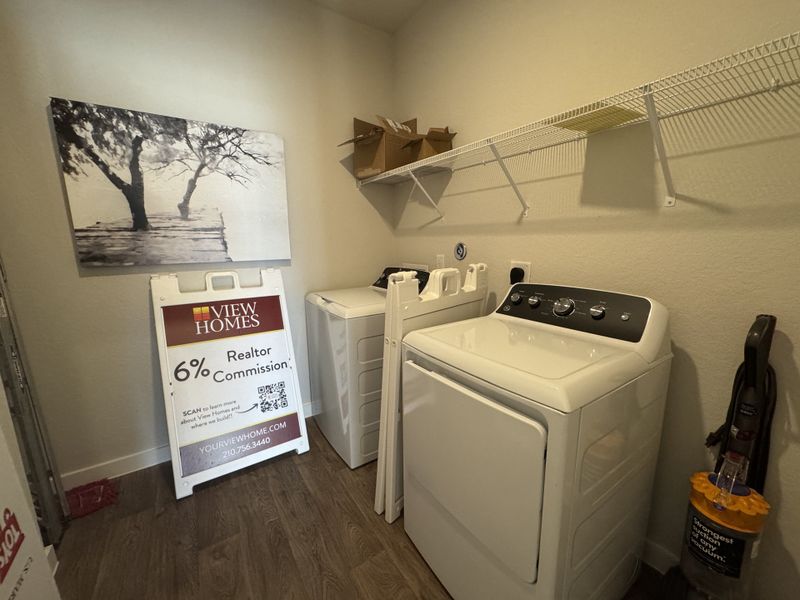A functional laundry room featuring a washer, dryer, shelving, and stylish art, perfect for efficient home chores. A functional laundry room featuring a washer, dryer, shelving, and stylish art, perfect for efficient home chores.