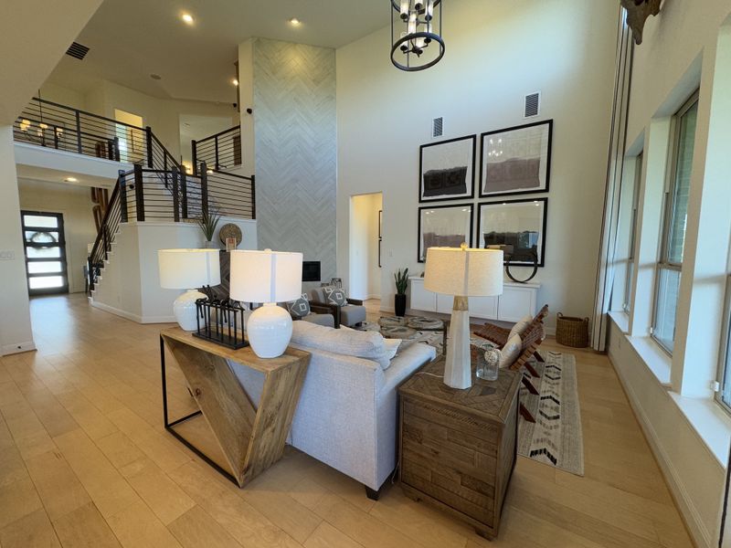 A spacious living room with high ceilings, modern decor, large windows, and a stylish staircase. A spacious living room with high ceilings, modern decor, large windows, and a stylish staircase.