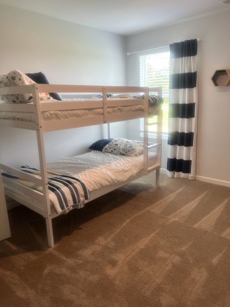 Cozy bedroom with white bunk beds, striped curtains, and soft carpeting for a welcoming atmosphere.