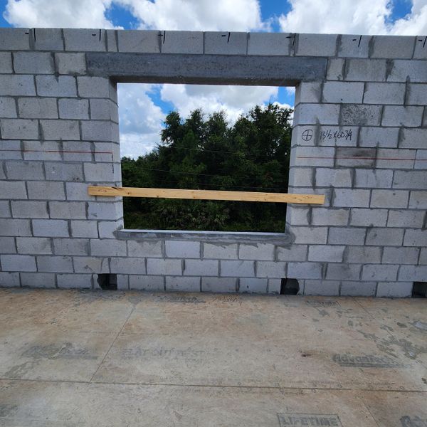 A concrete block construction with open window framing lush greenery, showcasing future potential in Palm Bay by D.R. Horton (Palm Bay, FL).