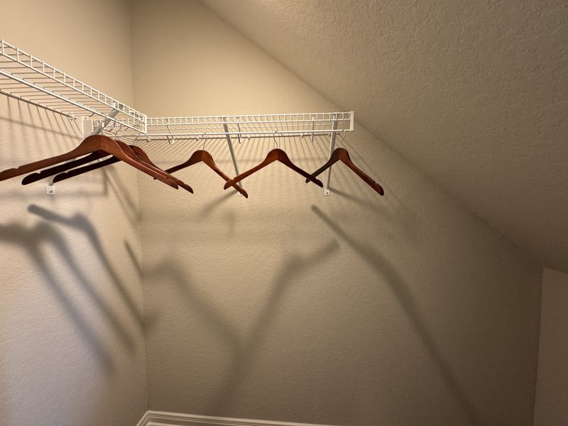 A cozy walk-in closet with angled ceiling, featuring wooden hangers and white wire shelving.