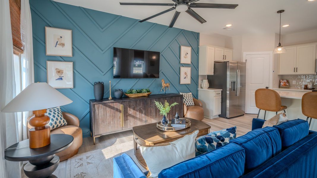 Living area with ceiling fan, accent wall, and access to kitchen