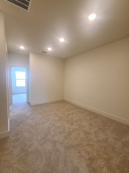 A cozy room with plush carpeting, recessed lighting, and neutral walls leading to a bright adjoining space.