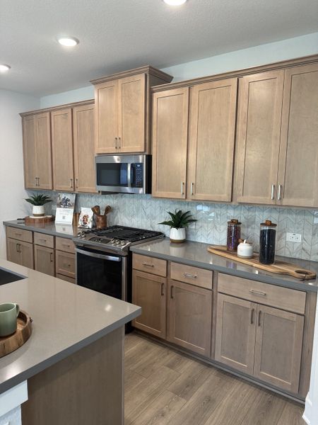 A modern kitchen featuring light wood cabinetry, sleek countertops, and a chic backsplash with integrated appliances.