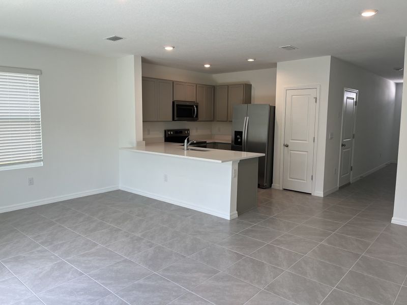 A modern kitchen with sleek gray cabinetry, stainless appliances, and an open floor plan with tile flooring.