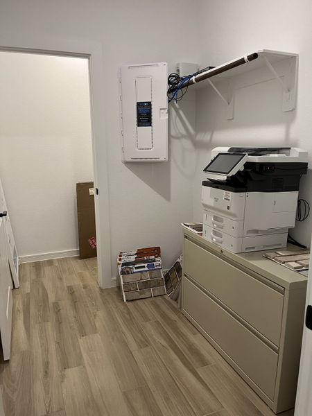 A sleek utility room with light wood flooring, a filing cabinet, printer, and organized shelving. A sleek utility room with light wood flooring, a filing cabinet, printer, and organized shelving.